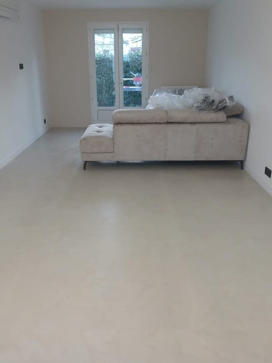 Séjour au carrelage clair et net, canapé d'angle face à la porte-fenêtre sur jardin