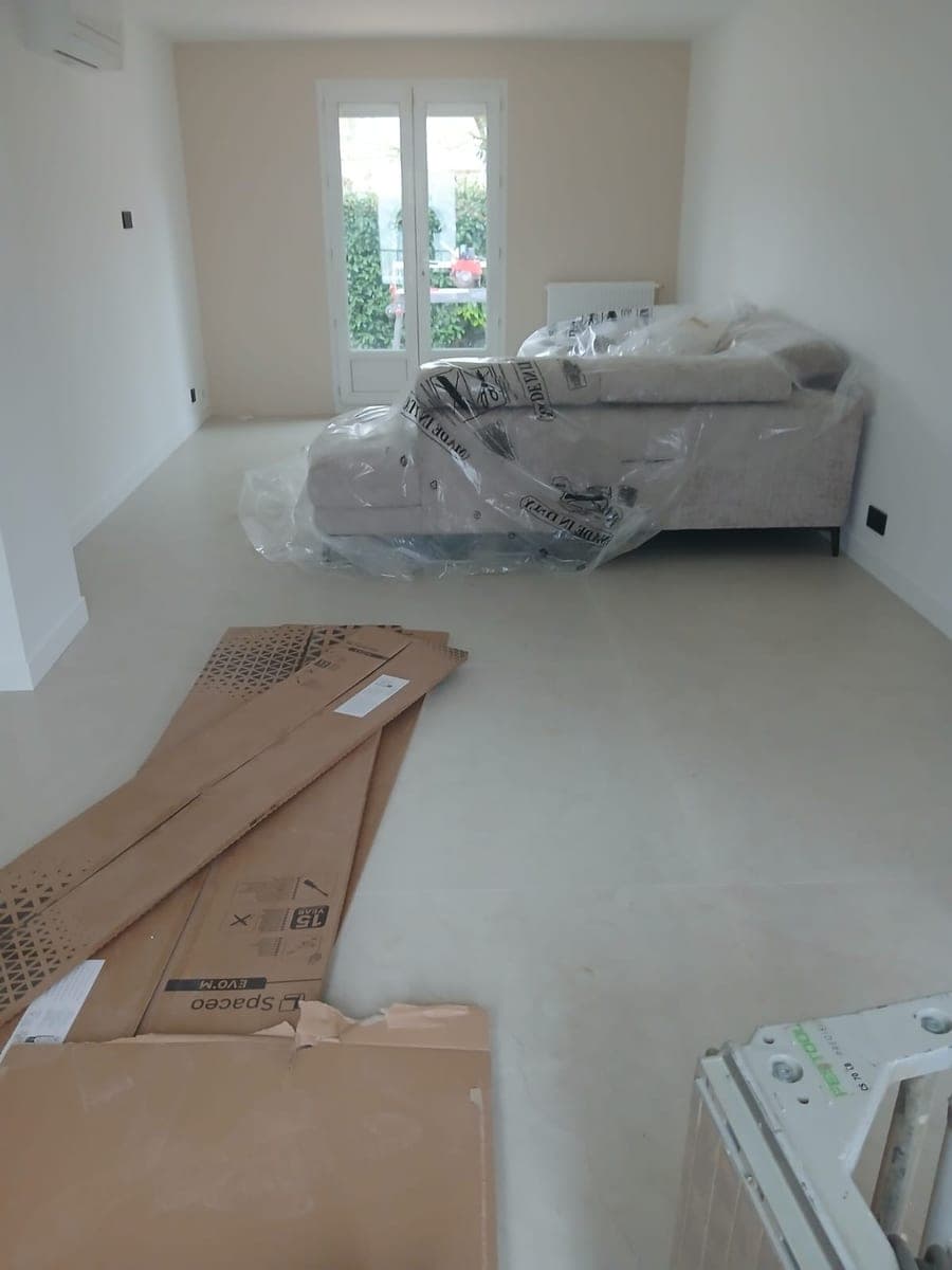 Séjour en fin de travaux, panneaux de carton au sol et canapé encore sous film plastique