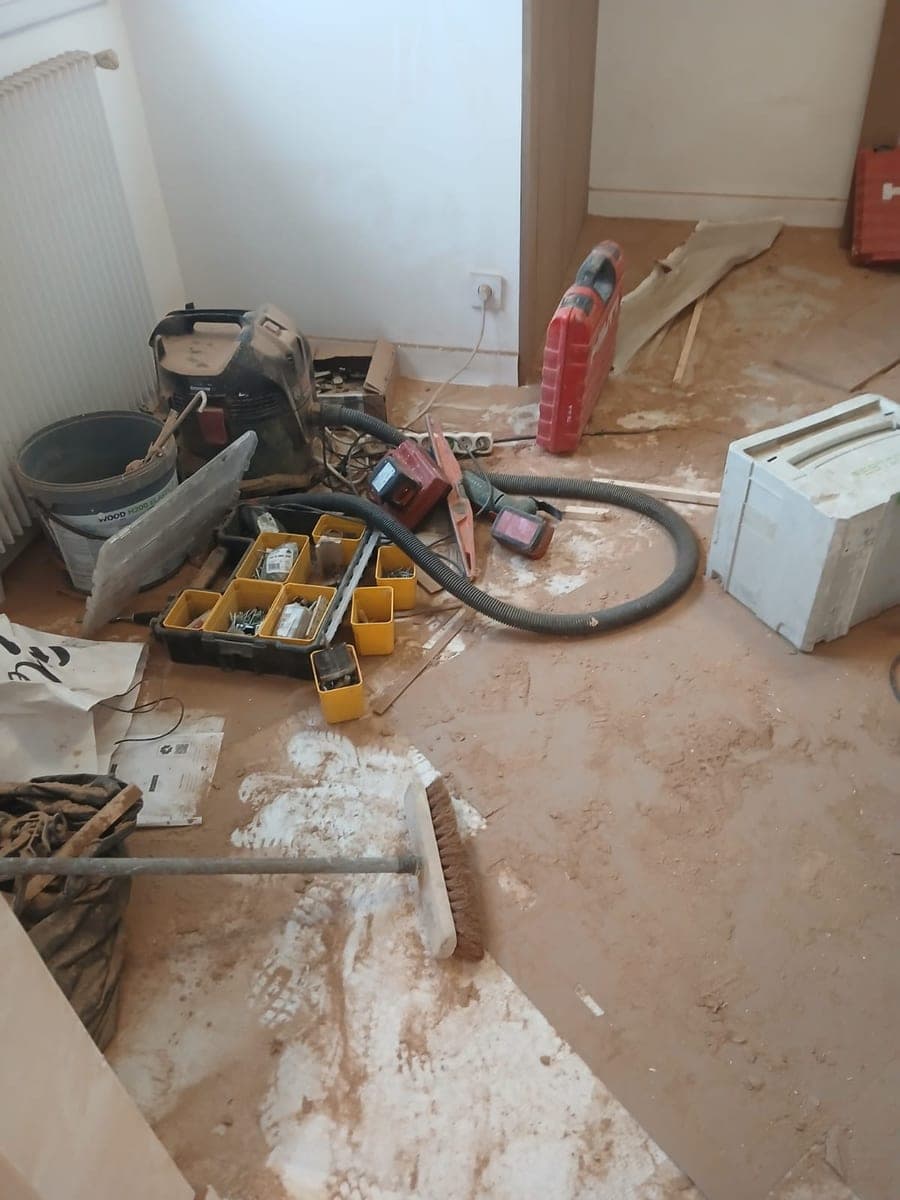 Sol couvert de poussière de plâtre, aspirateur de chantier et caisses d'outils dans une pièce en travaux