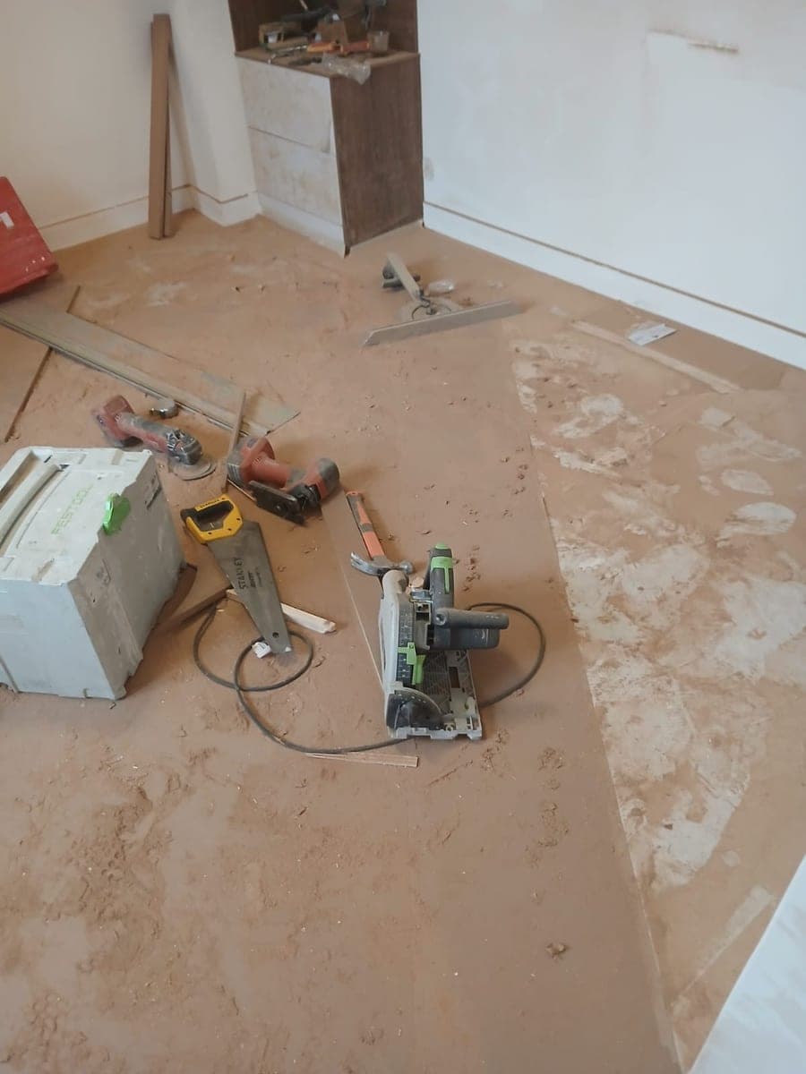 Plancher blanchi par la poussière, scie et coffrets d'outillage posés au sol en cours de rénovation