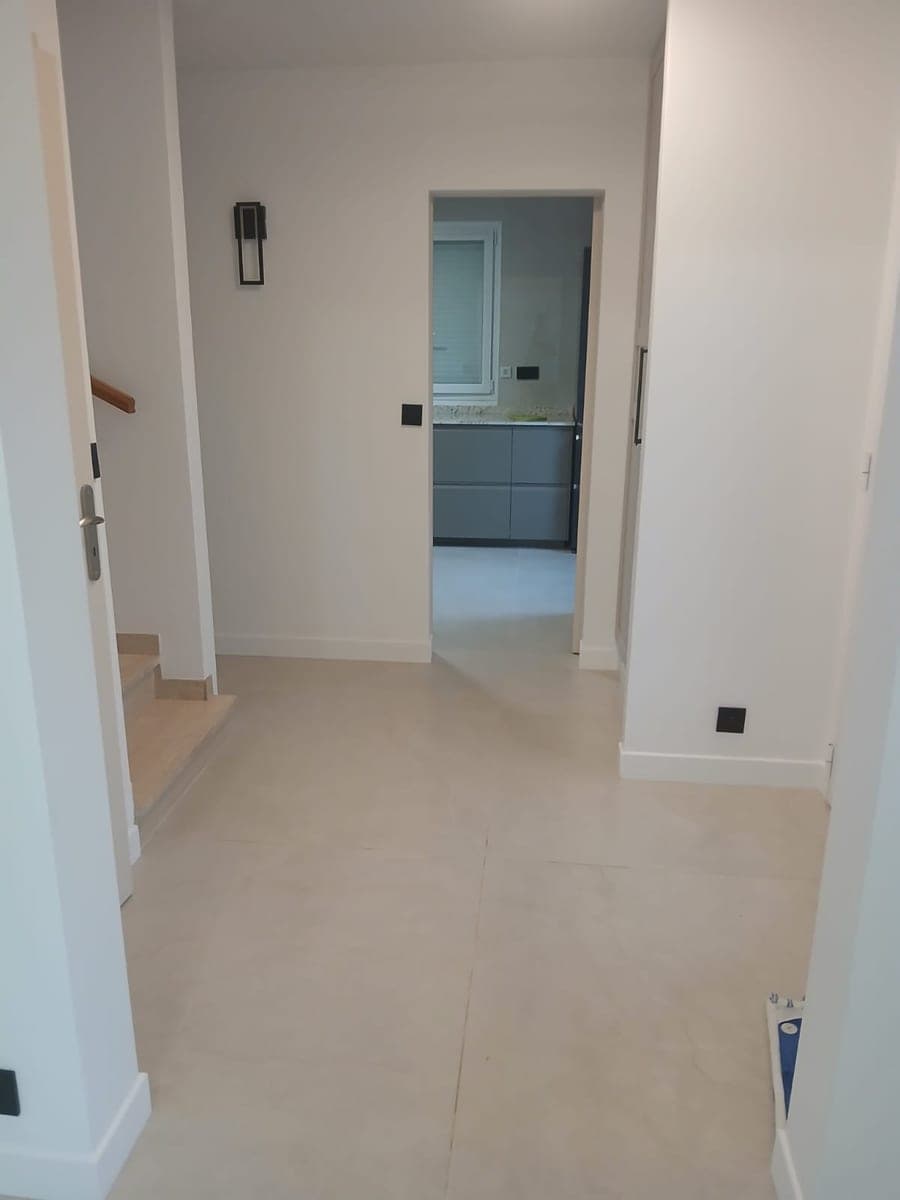 Entrée lumineuse au carrelage clair, départ d'escalier et vue sur la cuisine