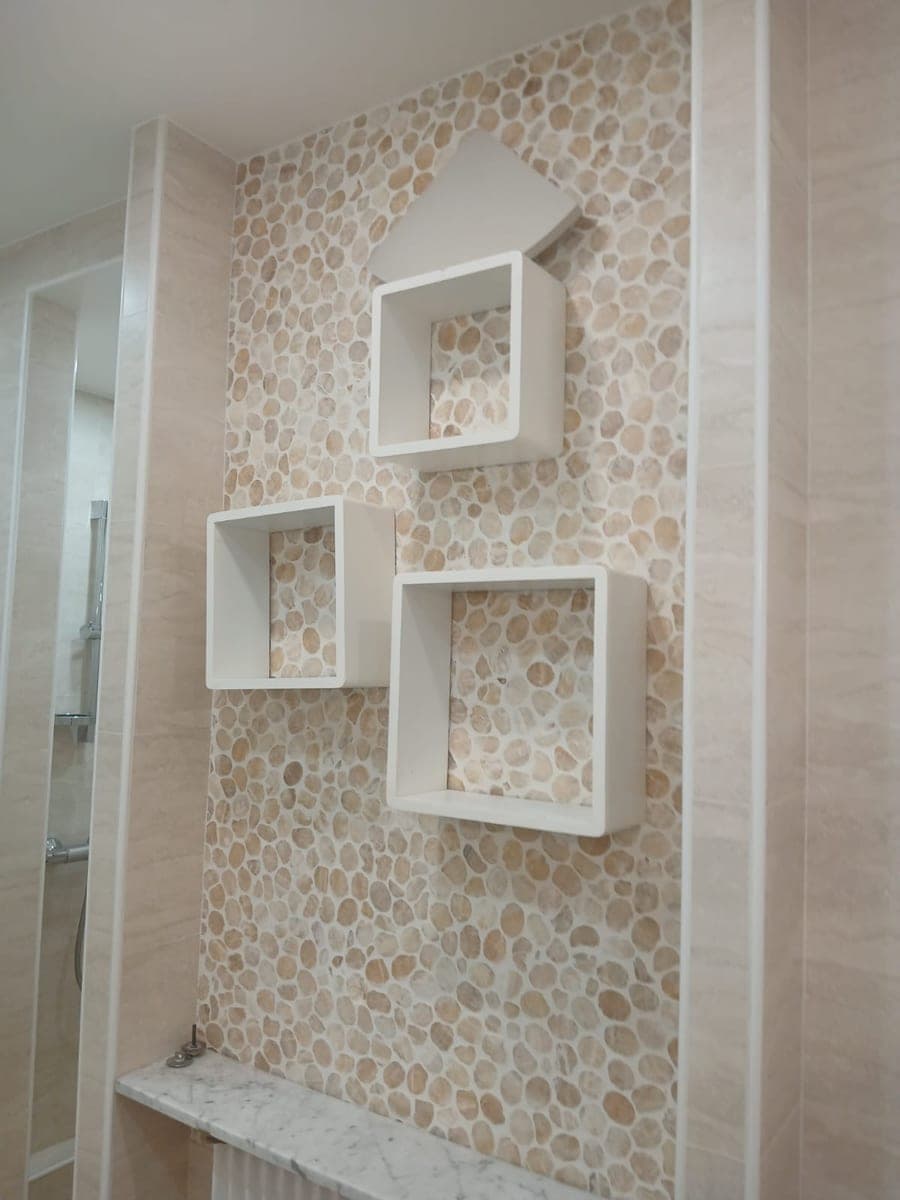 Mur de galets clairs et niches blanches en relief au-dessus d'une baignoire