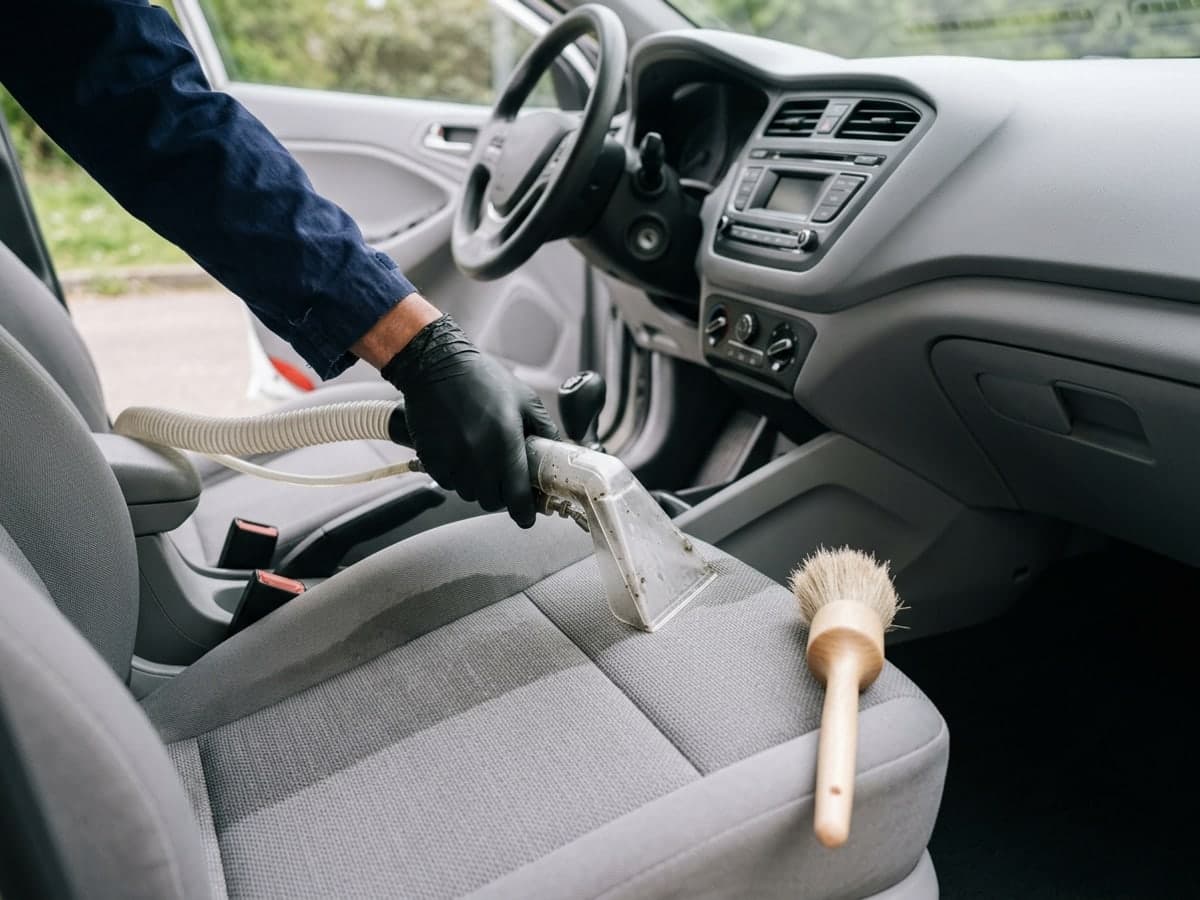 Buse d'extraction sur le siège conducteur en tissu gris d'une voiture, pinceau de détailing posé à côté