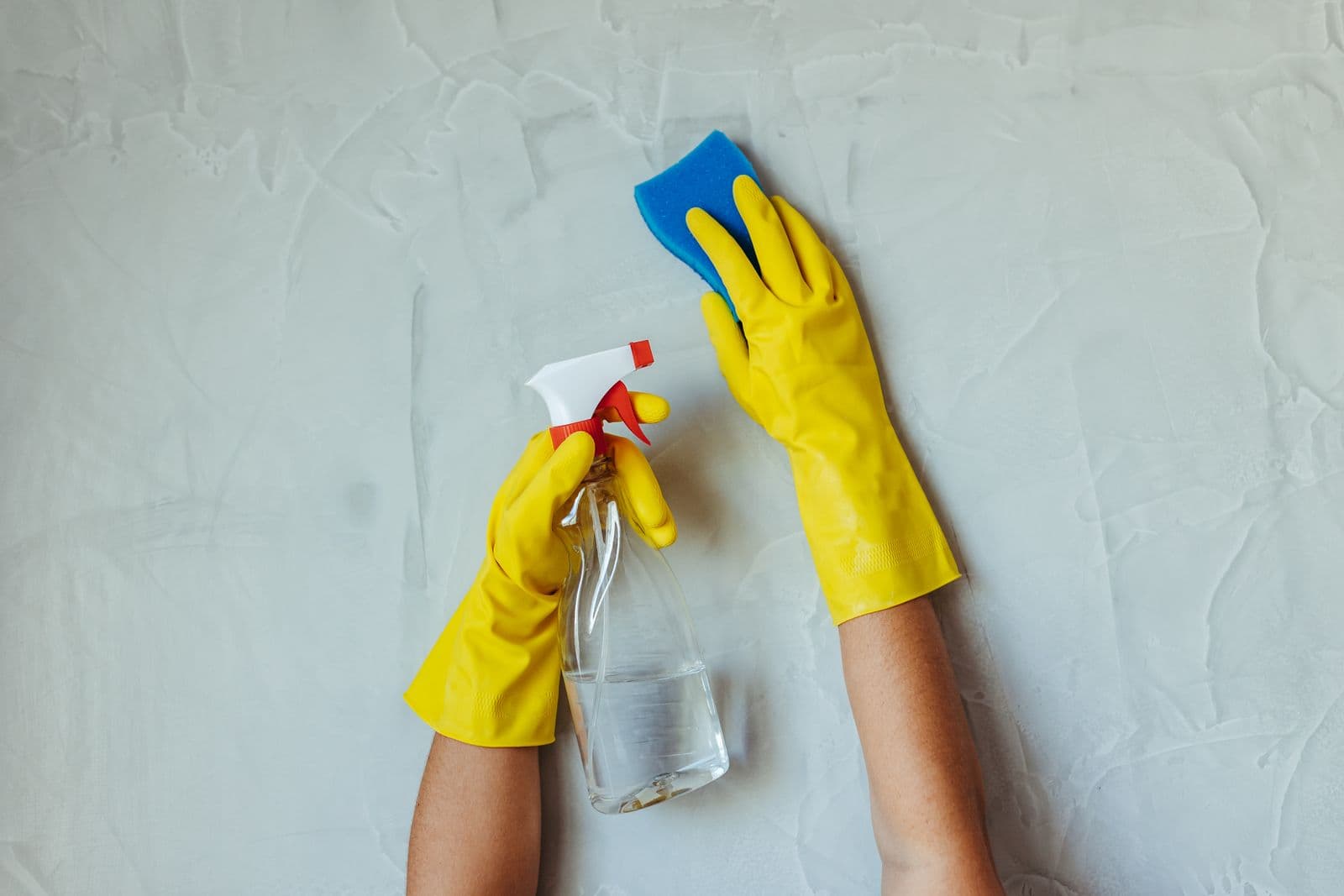 Gants jaunes lessivant un mur à l'éponge et au spray