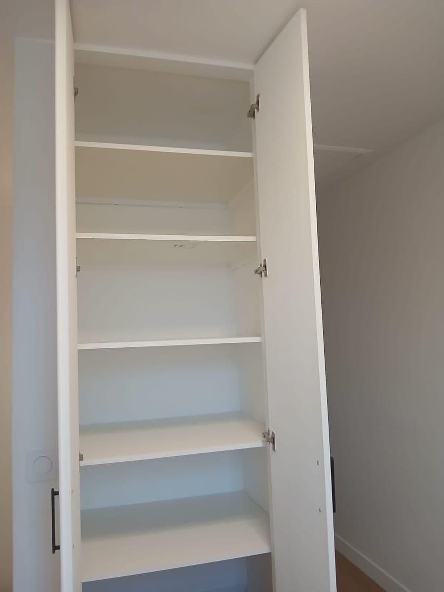 Grande armoire blanche ouverte, étagères vides dépoussiérées