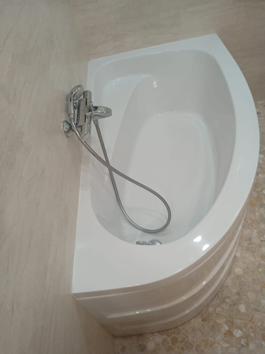 Baignoire d'angle blanche et robinet chromé, sol en galets clairs